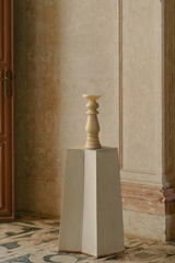 Decorative candle on a pedestal in a room with a wooden door and patterned floor.